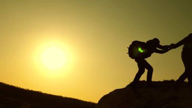 iş halkının takım çalışması. yolcular kayadan diğerine tırmanır. ortak iş. Yavaş hareket. Climbers siluetleri birbirlerine ellerini streç, tepenin üstüne tırmanma.