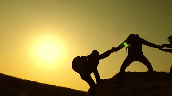 Lavoro di squadra di uomini d'affari. i viaggiatori si arrampicano uno dopo l'altro sulla roccia. affari congiunti. Al rallentatore. Silhouette scalatori allungano le mani l'una all'altra, salendo in cima alla collina . — Foto Stock