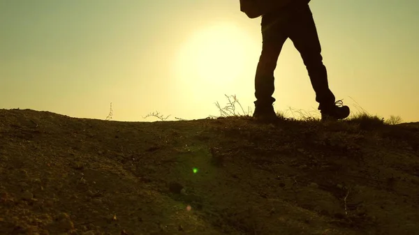 Um homem-viajante corajoso, subindo ao topo de uma montanha, caminhando ao longo de um caminho ao longo de uma crista rochosa perigosa. Parede íngreme que abre uma bela vista do pôr do sol. câmara lenta. close-up . — Fotografia de Stock