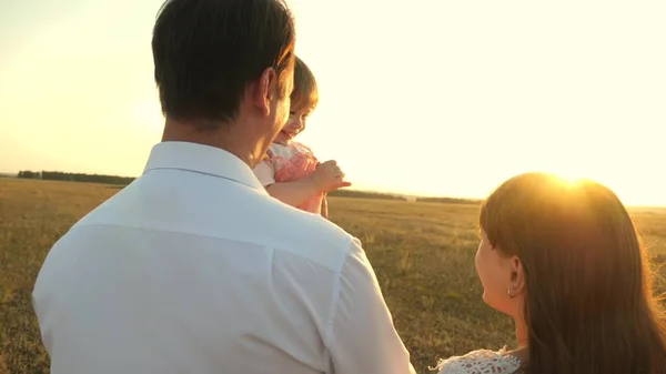 Padre con figlie che riposano nel parco. concetto di famiglia felice e infanzia. La famiglia gioca con il bambino al tramonto. Papà e mamma camminano con sua figlia tra le braccia al tramonto . — Foto Stock
