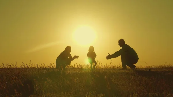 Matka i tata bawią się z córką na słońcu. szczęśliwy dziecko idzie z tata do Mamo młodą rodzinę na polu z dzieckiem 1 rok. koncepcji szczęścia rodzinnego. piękne słońce, zachód słońca. — Zdjęcie stockowe