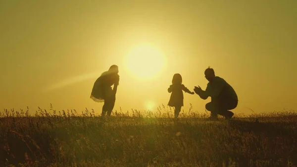 Мати і тато грають зі своєю донькою на сонці. щаслива дитина йде від тата до мами. молода сім'я в полі з дитиною 1 рік. концепція сімейного щастя. красиве сонце, захід сонця . — стокове фото