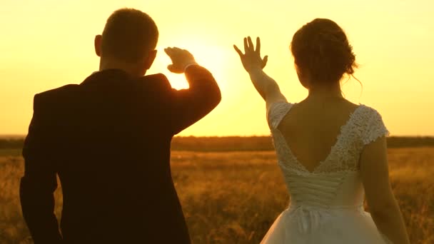 Un hombre y una mujer muestran un corazón con sus manos al atardecer del sol dorado. Amantes en un viaje romántico. Trabajo en equipo de una pareja amorosa. El concepto de una familia feliz. Primer plano . — Vídeo de stock