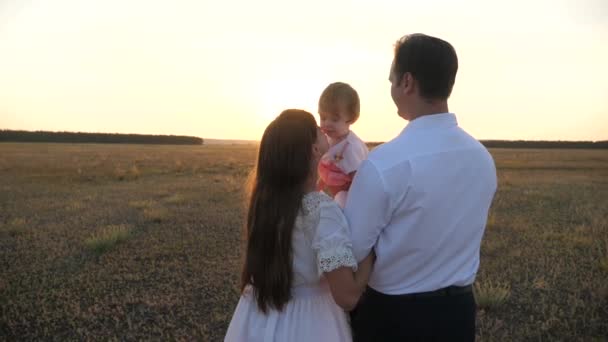 La familia juega con el bebé al atardecer. Papá y mamá caminan con su hija en brazos al atardecer. padre con hijas descansando en el parque. concepto de familia feliz y la infancia . — Vídeos de Stock