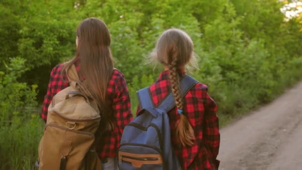 Genç kızlar seyahat sırt çantaları el el. turistler çocuklar ülke yolu boyunca gitmek. Mutlu aile tatile seyahat. Spor turizmi konsepti. — Stok video