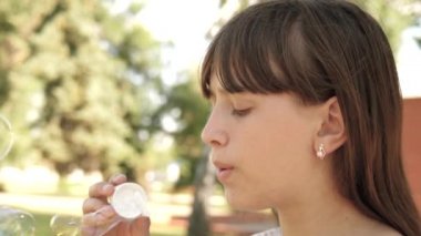 mutlu kız parkta Bahar, yaz ve gülümseyen güzel sabun köpüğü üfleme. Ağır çekim. Genç Kız parkta şehrin içinden seyahat.