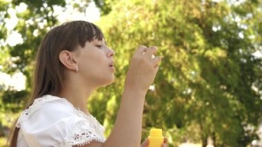 mutlu kız parkta Bahar, yaz ve gülümseyen güzel sabun köpüğü üfleme. Ağır çekim. Genç Kız parkta şehrin içinden seyahat.