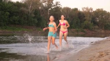 sahil boyunca koşan mutlu çocuklar. Kızlar sahilde kum boyunca kumda koşarlar su damlaları sıçratıyor ve gülüyorlar. Yaz tatilinde mutlu ve özgür gençler gün batımında dinlenirler. Takım çalışması