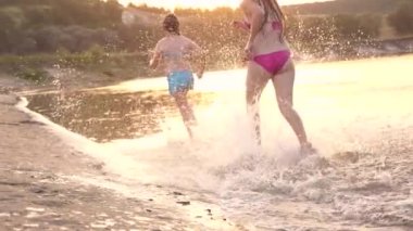 sahil boyunca koşan mutlu çocuklar. Kızlar sahilde kum boyunca kumda koşarlar su damlaları sıçratıyor ve gülüyorlar. Yaz tatilinde mutlu ve özgür gençler gün batımında dinlenirler. Takım çalışması
