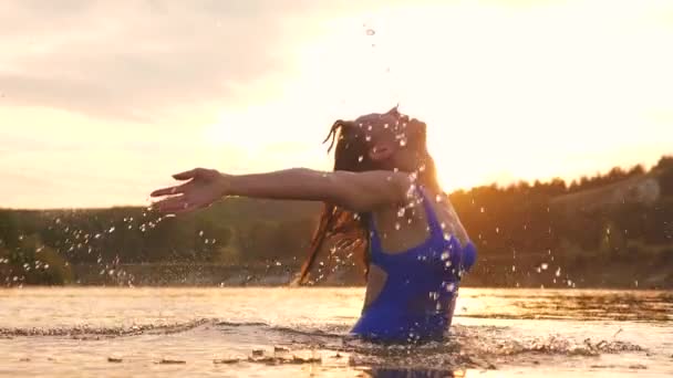 Menina vira o cabelo para trás. belo borrifo de água em raios de pôr-do-sol, um respingo de água em raios do sol. ela asperge refrescante água do rio com seu cabelo longo na noite de verão perto da ilha tropical . — Vídeo de Stock