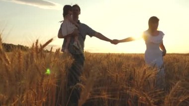 Çocuklu mutlu genç aile buğday tarlasında yürüyor. baba kız ve anne sahada oynuyorlar. Annem ve babam bir buğday tarlasında el ele tutuşuyorlar. Yavaş çekim.