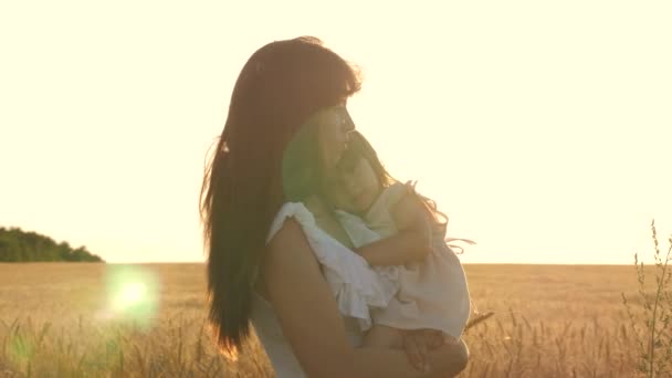 Feliz mamá camina con el bebé en sus brazos en un campo con trigo. La hija sostiene a mamá junto al pecho. La familia está viajando . — Vídeo de stock