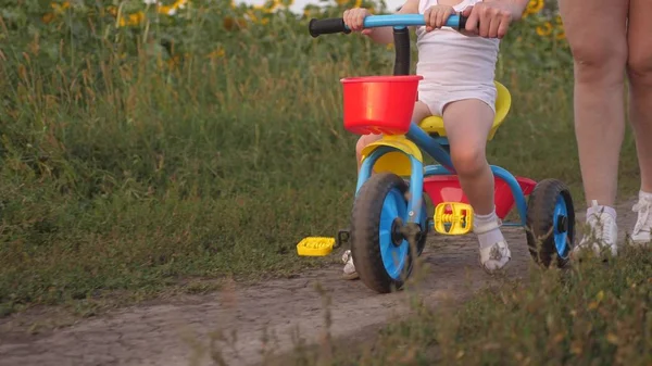 A mãe ensina a filha a andar de bicicleta. close-up. A mãe brinca com a filha. uma criança pequena aprende a andar de bicicleta. conceito de infância feliz . — Fotografia de Stock