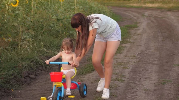 Moeder leert dochter om een fiets te rijden. Zuster speelt met een klein kind. Het concept van Happy Childhood. een klein kind leert om een fiets te rijden. — Stockfoto