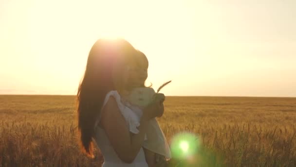 Mamá y su hijita están caminando a lo largo de un camino rural en un campo de trigo. madre y bebé camina en la naturaleza. Mamá feliz camina con el bebé en sus brazos. Hija sostiene mamá por el pecho . — Vídeos de Stock