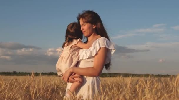 Kleine dochter kusjes moeder op een tarwe veld. gelukkige familie reist. baby in de armen van de moeder. moeder wandelingen met de baby in het veld Hold spikeletten met tarwe in de hand. Gelukkig familieconcept. — Stockvideo