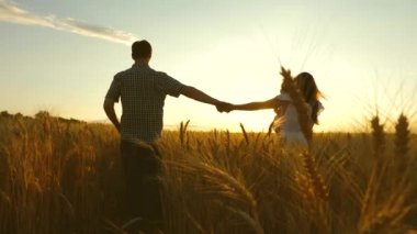 Anne çocuk ve baba el ele tutuşarak bir buğday tarlasında yürüyorlar. baba kız ve anne sahada oynuyorlar. Yavaş çekim. Çocuklu mutlu genç aile buğday tarlasında yürüyor.