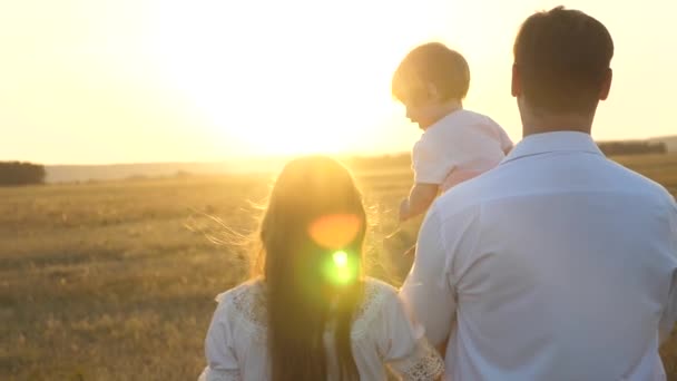 Pappa och mamma går med sin dotter i famnen vid solnedgången. familjevandringar med ett barn vid solnedgången. Fader med döttrar som vilar i parkera. begreppet lycklig familj och barndom. — Stockvideo