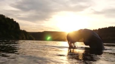 neşeli kız ferahlatıcı bir nehir suyu ile tropikal adanın yakınında ferahlatıcı bir yaz akşamı onu uzun saçları sıçraması. Kız geri saç çevirir. gün batımı ışınları su güzel sprey. su sıçrama