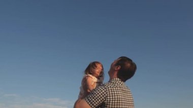 Baba ve küçük çocuk birlikte oynuyorlar, gülüyorlar ve sarılıyorlar. Babam mavi gökyüzüne mutlu bir kız çocuğu fırlatıyor. Mutlu aile seyahatleri. Bebeğin ebeveynin kollarında olması. Baba izinli. Mutlu aile kavramı.