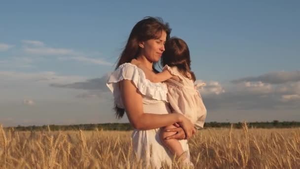 Mamma går med barnet i fältet hålla spikelets med vete i handen. lilla dotter kysser mamma på ett vetefält. lyckliga familjeresor. Baby i armarna på mamma. Happy familjekoncept. — Stockvideo