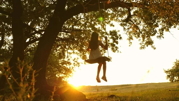 Kind reitet eine Seilschaukel auf einem Eichenzweig im Wald. Mädchen lacht, freut sich. junges Mädchen, das auf einer Schaukel unter einem Baum in der Sonne schwingt und mit Kindern spielt. Nahaufnahme. Familienspaß im Park, in der Natur. — Stockfoto