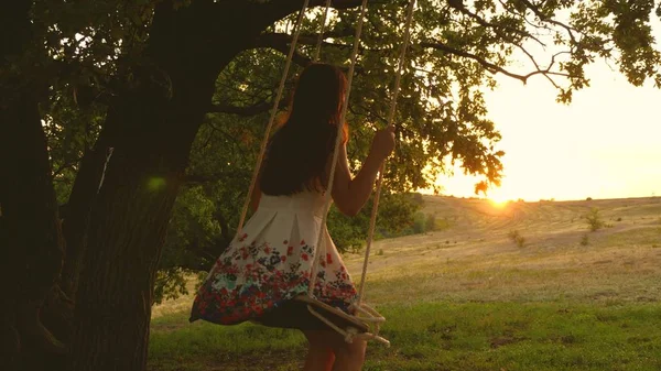 Adolescent fille bénéficie d'un vol sur une balançoire un soir d'été dans la forêt. jeune fille se balançant sur une balançoire de corde sur une branche de chêne. Belle fille dans une robe blanche dans le parc . — Photo