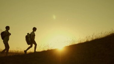 sırt çantaları ile çocuklar ve anne güneşte dağa tırmanmak seyahat. Anne ve kızları kampa gidiyor. Gün batımında seyahat eden çocukları olan turist ailesi. turistlerin ortak çalışma. zafere hareket. Yavaş