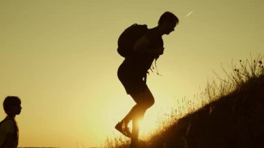 baba çocukların dağa tırmanmasını yardım elini tutar. Gün batımında seyahat eden çocukları olan turist ailesi. baba, çocuklar ve sırt çantaları ile anne seyahat güneşte dağtırmanmak. turistik ekip çalışması