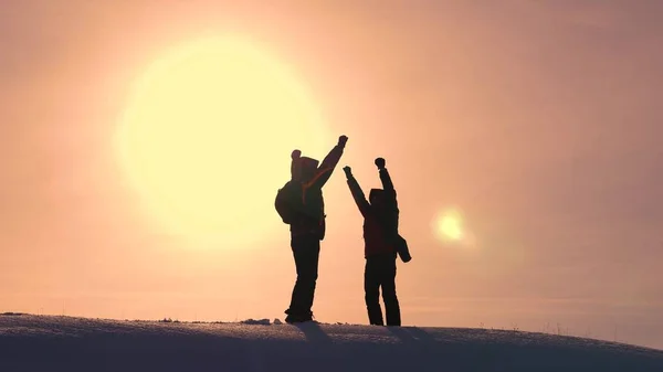 I turisti arrivano in cima alla collina innevata e si rallegrano della vittoria sullo sfondo di un tramonto giallo. viaggiatori incontrati in cima al successo. lavoro di squadra e vittoria. turismo ecologico — Foto Stock