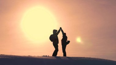 Turistler karlı tepenin üstüne gelir ve sarı bir günbatımı zemin karşı zafer sevinirler. gezginler başarı üstünde bir araya geldi. takım çalışması ve zafer. ekolojik turizm