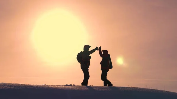 Οι τουρίστες έρχονται στην κορυφή του χιονισμένο λόφο και χαίρονται στη νίκη με φόντο ένα κίτρινο ηλιοβασίλεμα. ταξιδιώτες συναντήθηκαν στην κορυφή της επιτυχίας. ομαδική δουλειά και νίκη. οικολογικού τουρισμού — Φωτογραφία Αρχείου
