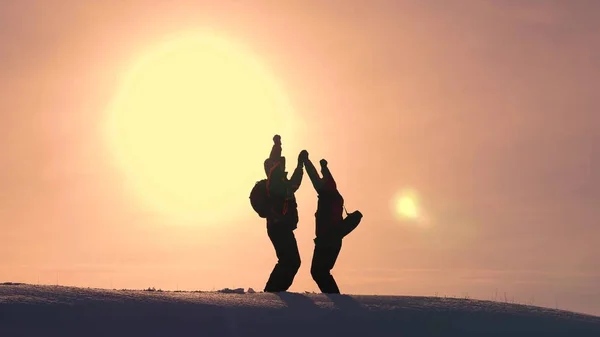 Tourists come to top of snowy hill and rejoice at victory against backdrop of a yellow sunset. travelers met on top of success. teamwork and victory. ecological tourism