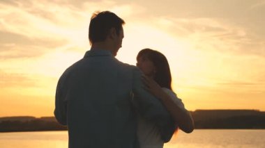 Genç çift sahilde gün batımında dans ediyor. Sevgi dolu erkek ve kadın gölün arka planda güneşin parlak ışınları dans. Yaz parkında akşam mutlu adam ve kız vals.