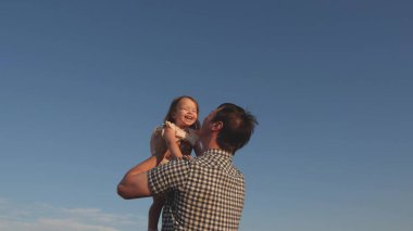 Babam mavi gökyüzüne mutlu bir kız çocuğu fırlatıyor. Baba ve küçük çocuk birlikte oynuyorlar, gülüyorlar ve sarılıyorlar. İyi yolculuklar. Bebeğin ebeveynin kollarında olması. Baba izinli. Mutlu aile kavramı..