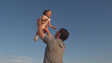 Babam mavi gökyüzüne mutlu bir kız çocuğu fırlatıyor. Baba ve küçük çocuk birlikte oynuyorlar, gülüyorlar ve sarılıyorlar. İyi yolculuklar. Bebeğin ebeveynin kollarında olması. Baba izinli. Mutlu aile kavramı..