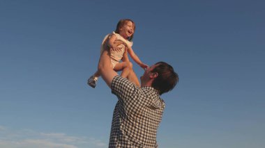Babam mavi gökyüzüne mutlu bir kız çocuğu fırlatıyor. Baba ve küçük çocuk birlikte oynuyorlar, gülüyorlar ve sarılıyorlar. İyi yolculuklar. Bebeğin ebeveynin kollarında olması. Baba izinli. Mutlu aile kavramı..