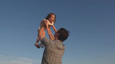 Babam mavi gökyüzüne mutlu bir kız çocuğu fırlatıyor. Baba ve küçük çocuk birlikte oynuyorlar, gülüyorlar ve sarılıyorlar. İyi yolculuklar. Bebeğin ebeveynin kollarında olması. Baba izinli. Mutlu aile kavramı..