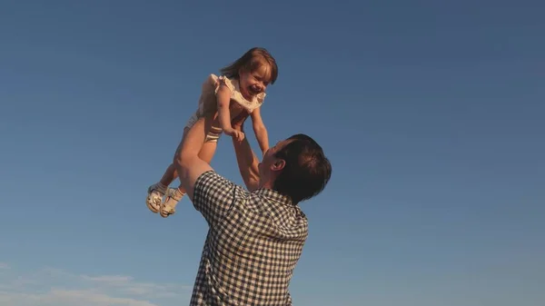 Papa wirft eine glückliche Tochter in den blauen Himmel. Vater und Kind spielen, lachen und umarmen sich. Glückliche Familienreisen. Baby in den Armen der Eltern. Vatertag frei. Das Konzept einer glücklichen Familie. — Stockfoto