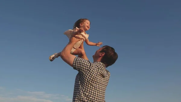 Pappa spyr upp en lycklig dotter i den blå himlen. Far och barn leker, skrattar och kramas tillsammans. Lyckliga familjeresor. Barnet i armarna på föräldern. Pappa är ledig idag. Begreppet lycklig familj. — Stockfoto