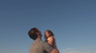 Baba ve küçük çocuk birlikte oynuyorlar, gülüyorlar ve sarılıyorlar. Babam mavi gökyüzüne mutlu bir kız çocuğu fırlatıyor. Mutlu aile seyahatleri. Bebeğin ebeveynin kollarında olması. Baba izinli. Mutlu aile kavramı.