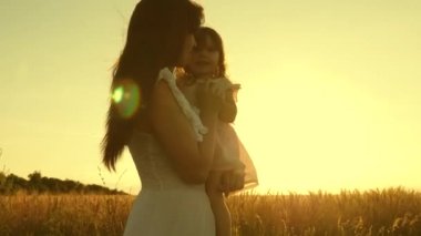 anne ve küçük kızı güneşin üzerinde olgun buğday bir alanda oynuyorlar. anne buğday ile bir alanda bir çocuk ile yürür. mutlu aile seyahatleri. annemin kollarında bebek. mutlu aile kavramı.
