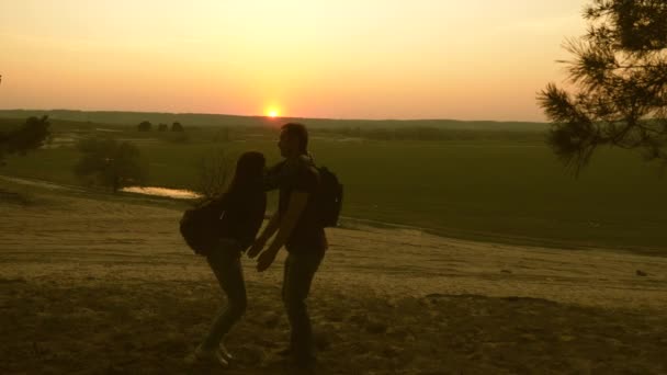Resenärer en man och en kvinna dansar och gläds. man håller sin älskade kvinna i sina armar i solnedgången ljus. Teamwork resenärer med ryggsäckar. kärleksfullt par på semester. Hiker flicka. Slow motion. — Stockvideo