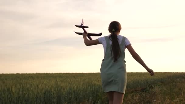 快乐的女孩在麦田里用玩具飞机跑步。孩子们玩玩具飞机。青少年梦想飞行,并成为一名飞行员。这个女孩想成为一名飞行员和宇航员. — 图库视频影像