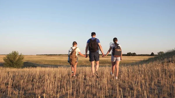 Family of tourists on journey. Dad with two daughters on a camping trip. children and father with backpacks are walking through field. teamwork of tourists. movement towards intended goal and victory. — Stock Photo, Image