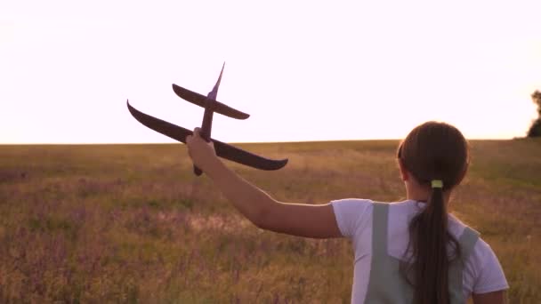 Jovem corre com um avião de brinquedo no campo nos raios de estilingue. As crianças brincam de avião de brinquedo. adolescente sonha em voar e se tornar um piloto. a menina quer se tornar um piloto e astronauta . — Vídeo de Stock