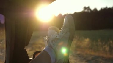 Araba camında bir kızın bacakları, güneşin parıltısı, kırsal yolda bir arabaya binme. Genç bir kadın açık bir pencereden bacaklarını koyarak, bir araba seyahat seviyor.