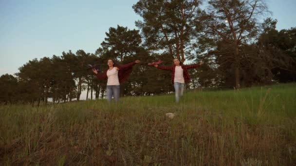 Sueños de volar. Concepto de infancia feliz. Dos chicas juegan con un avión de juguete al atardecer. Niños en el fondo del sol con un avión en la mano. Silueta de niños jugando en el avión — Vídeos de Stock