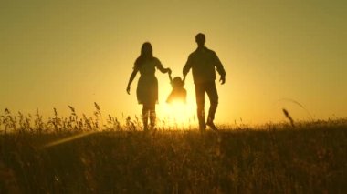 küçük kızı güneşin arka planda parkta baba ve anne el ele atlayarak. Aile konsepti. çocuk gün batımı ışığında sahada baba ve anne ile oynar. Doğada küçük bir çocukla yürümek.