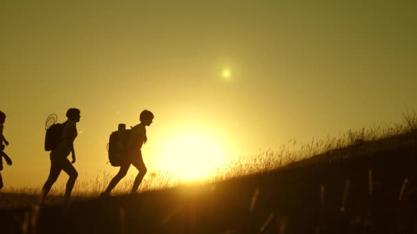 As crianças e a mãe com mochilas viajam escalam a montanha ao sol. Mãe e filhas vão acampar. Família de turistas com crianças viajando ao pôr do sol. trabalho conjunto dos turistas. movimento para a vitória . — Vídeo de Stock